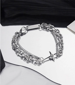 Detail of silver layered chain bracelet with a cross pendant on a reflective surface