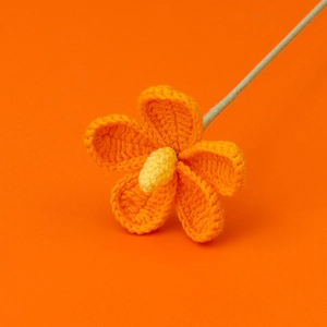 Close-up of handmade crochet flower with orange petals and yellow core on stems