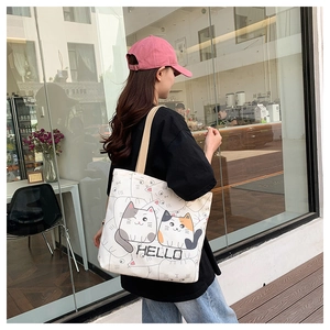Detail view of cream canvas tote bag featuring cute cartoon cats and Hello print