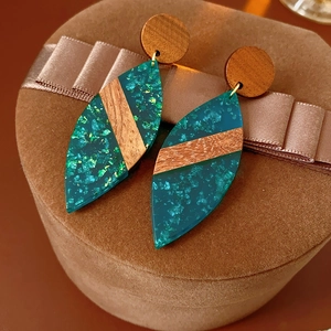 Détail de boucles d'oreilles en bois et résine pailletée verte sur ruban de satin