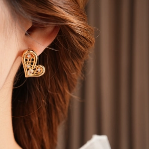 Close-up of golden hollow heart earrings with twisted edges and zircon inlay on model