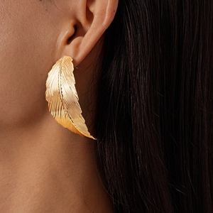Detailed view of leaf shaped gold earring featuring intricate metallic veins on a model