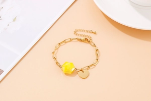 Detail of gold heart pendant bracelet with a faceted yellow bead on warm background