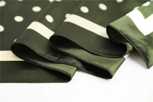 Detail of a folded dark green satin scarf with white polka dots and smooth silk texture