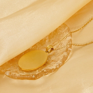 Elegant gold oval pendant necklace displayed on a textured glass tray with silk fabric