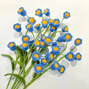 Close-up of handmade blue crochet lily of the valley flowers with green leaves