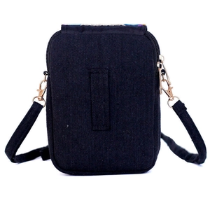 Detail of ethnic embroidery flap on black canvas bag showing metal zipper and belt loop
