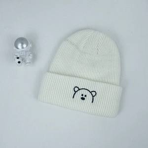 Detail of white ribbed knit beanie featuring a cute embroidered black bear on the folded cuff
