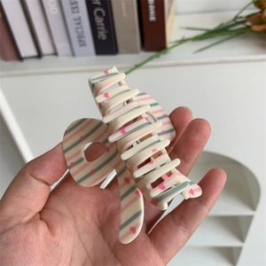 Detail of cream acrylic hair claw clip with pink stripes and tiny hearts pattern