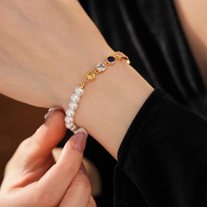 Detail eines Vintage-Perlenarmbands mit buntem Herz-Zirkon und Goldkette am Handgelenk