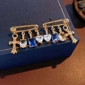 Macro detail of gold safety pin earrings with blue zircon heart and cross pendants
