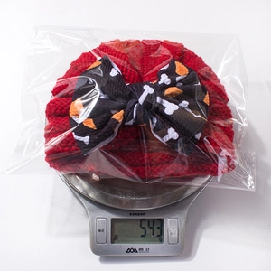 Detail shot of a red infant knit hat with bow on a scale showing 54.3g weight