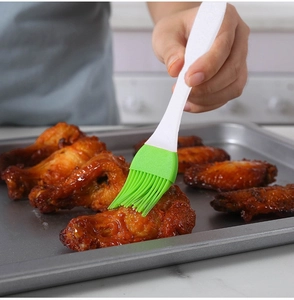 Silicone basting brush spreading sauce on grilled chicken wings in a kitchen setting