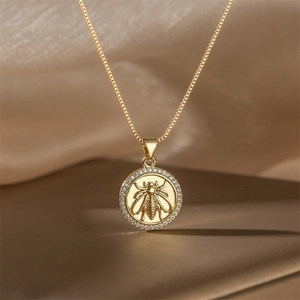 Close-up of a gold necklace with a bee-embossed circular pendant and pavé crystals
