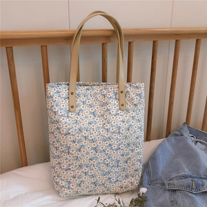 Détail d'un sac cabas fleuri avec des anses en cuir marron et des rivets en métal