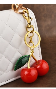 Close-up of a red cherry resin keychain with green leaves hanging on a white quilted bag