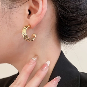 Close-up of golden C-shaped textured earrings worn by a model in formal attire