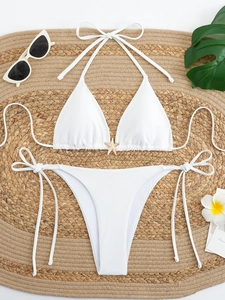Detail of white triangle bikini top with golden starfish accessory on woven mat