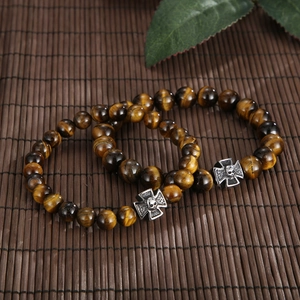 Close-up of tiger eye stone beads with silver skull cross pendants on bamboo mat