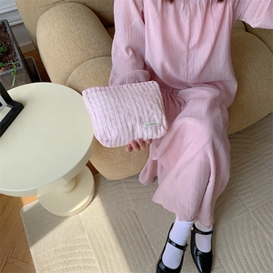 Pink and white checkered cosmetic bag held by a person on a soft beige sofa
