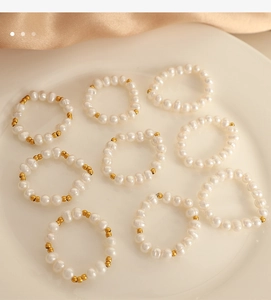 Dettaglio di anelli con perle barocche e perline dorate su un piatto di ceramica