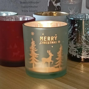 Close-up of frosted green glass Christmas candle holder with gold reindeer and tree patterns