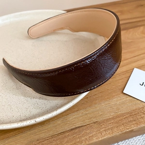 Detail of dark brown pleated leather headband with neat stitching on a beige ceramic plate