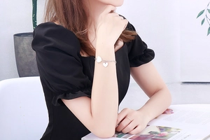 Détail d'un bracelet en chaîne argentée avec double pendentifs cœur sur une manchette noire