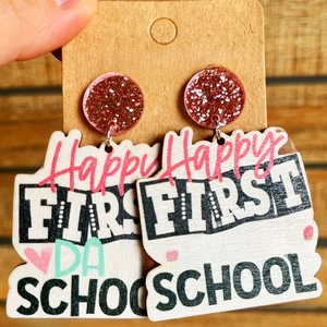 Close-up of wooden school earrings with pink sequins held on a jewelry card