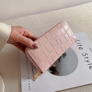 Detailed view of pink crocodile pattern long purse with gold zipper held by a model