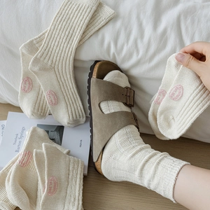 Calze in cotone lavorato a maglia crema con ricamo rosa su sfondo di letto bianco