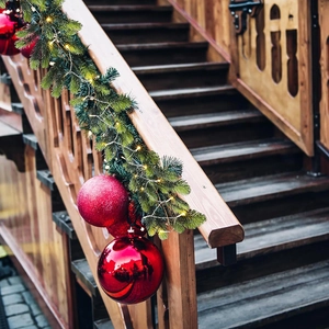 Close-up of 180cm flocked Christmas garland with red balls and warm LED lights on stairs