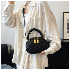 Black quilted crossbody bag with ruffled handle shown over a minimalist beige linen outfit.