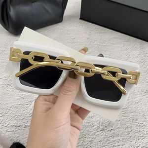 Detalle de gafas de sol blancas de gran tamaño con cadena dorada y estuche de primera