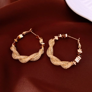 Détail de boucles d'oreilles créoles dorées géométriques sur fond velours rouge