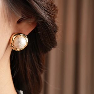 Close-up of a vintage gold-plated round earring with a large pearl on a model's ear