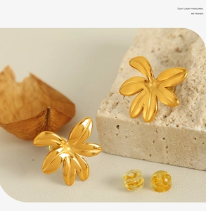 Detailed macro view of gold flower stud earrings with a matte texture on a natural stone base
