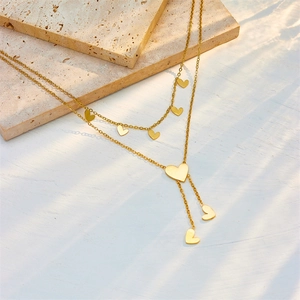 Minimalist double-layered gold heart tassel necklace on elegant stone and wood background