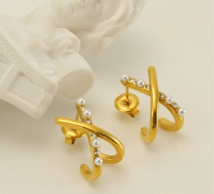 Macro shot of gold X-shaped crisscross earrings with pearls and zircon on stone