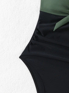 Detailed view of ruched side texture and olive green tie waist on a black swimsuit