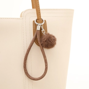 Porte-clés pompon en fourrure marron avec boucle tressée sur un sac à main beige