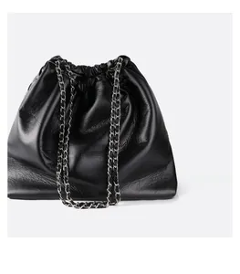 Close-up of black glossy leather drawstring bag with silver metal chain shoulder strap