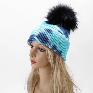 Detail of blue tie-dye knit beanie featuring a fluffy black pom-pom and wide folded cuff