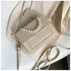 Detail of cream woven bag featuring oversized pearl handle and smooth leather strap