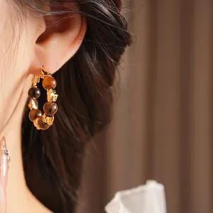 Boucles d'oreilles créoles en pierre œil de tigre plaquées or sur un modèle féminin