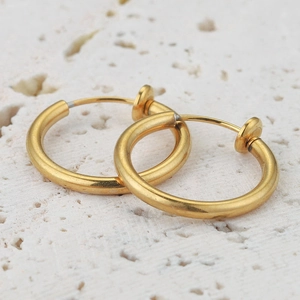Macro shot of gold non-pierced spring clip earrings on a white stone background