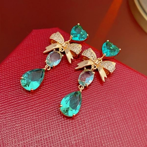 Detailed close-up of emerald bow earrings with zircons on a red leather gift box