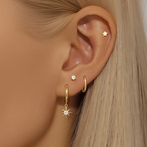 Close-up of gold star dangle earrings and stud set worn on ear for elegant style