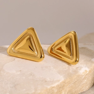 Nahaufnahme der geometrischen goldenen Dreieck-Ohrstecker auf beigefarbenem Naturstein