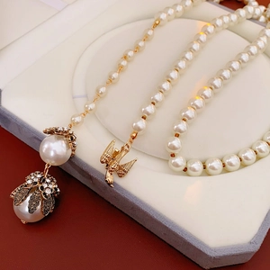 Detailed shot of pearl necklace with diamond-encrusted pendant and bird charm in jewelry box